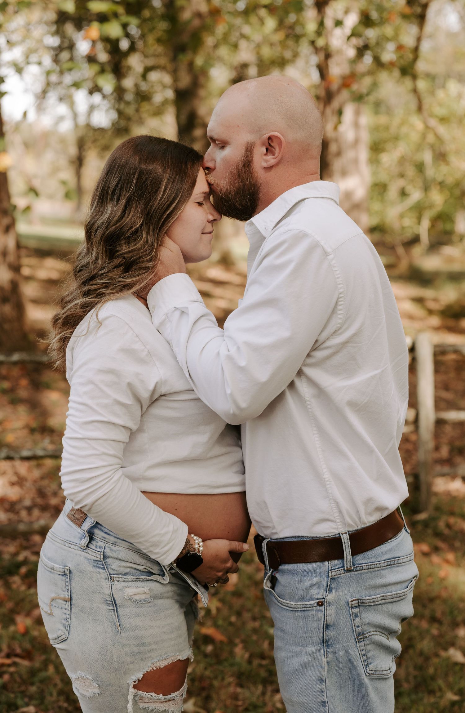 Couple in white tops and jeans embrace lovingly in an autumn outdoor setting.