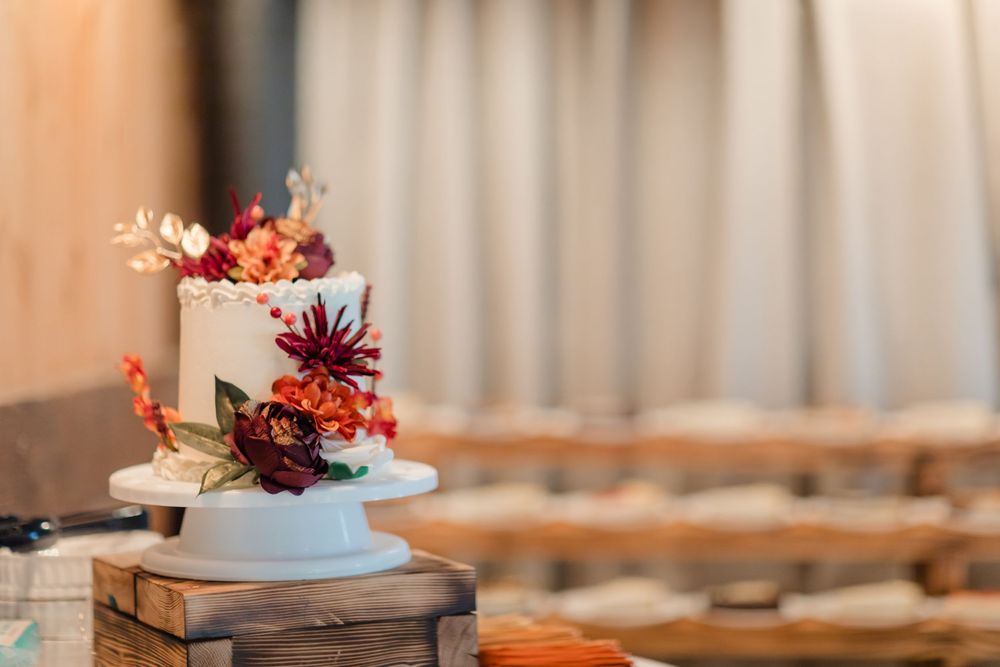Elegant white wedding cake with fresh flowers displayed on wooden stand at reception venue.