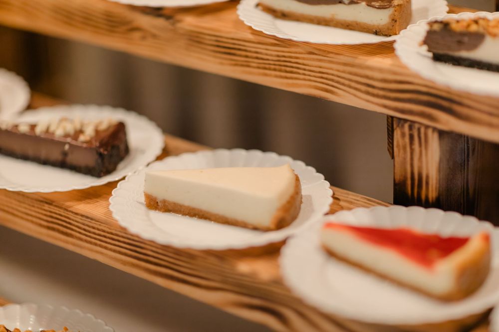A row of delicious looking white frosted cakes and pastries displayed on a wooden surface in warm lighting.