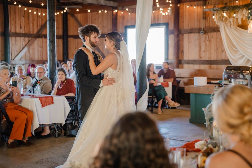 A couple shares their first dance at a rustic barn wedding reception decorated with string lights and white drapes.