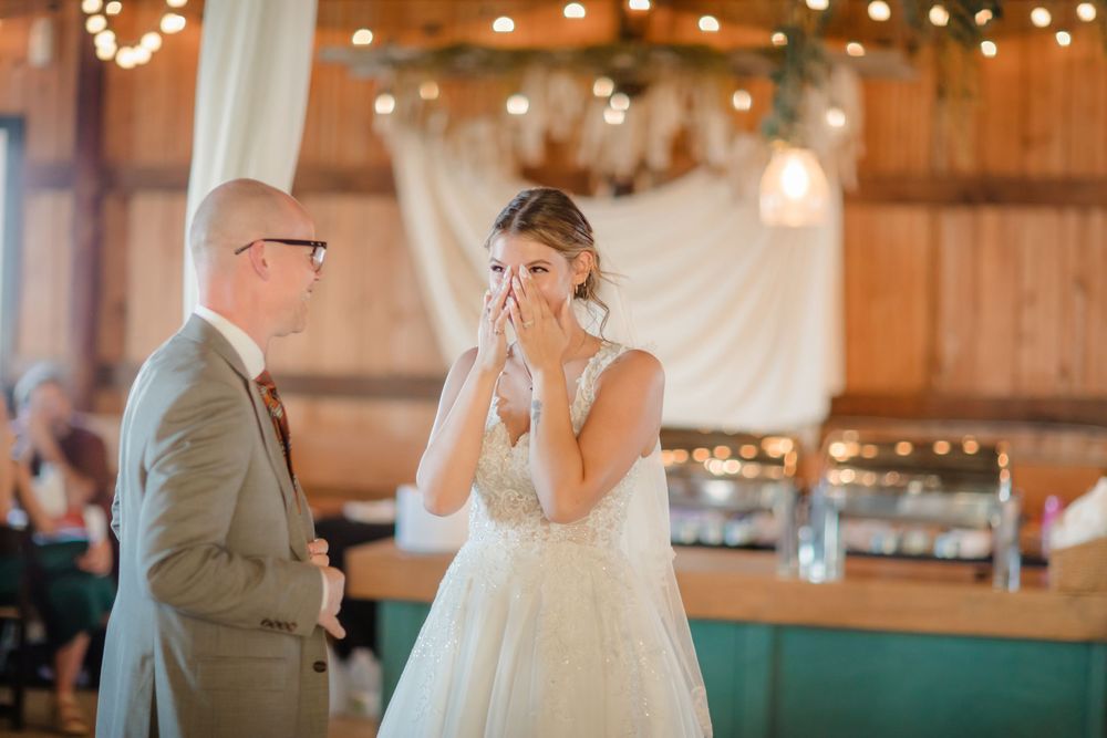 A couple shares an emotional first dance moment in a rustic barn venue decorated with string lights.