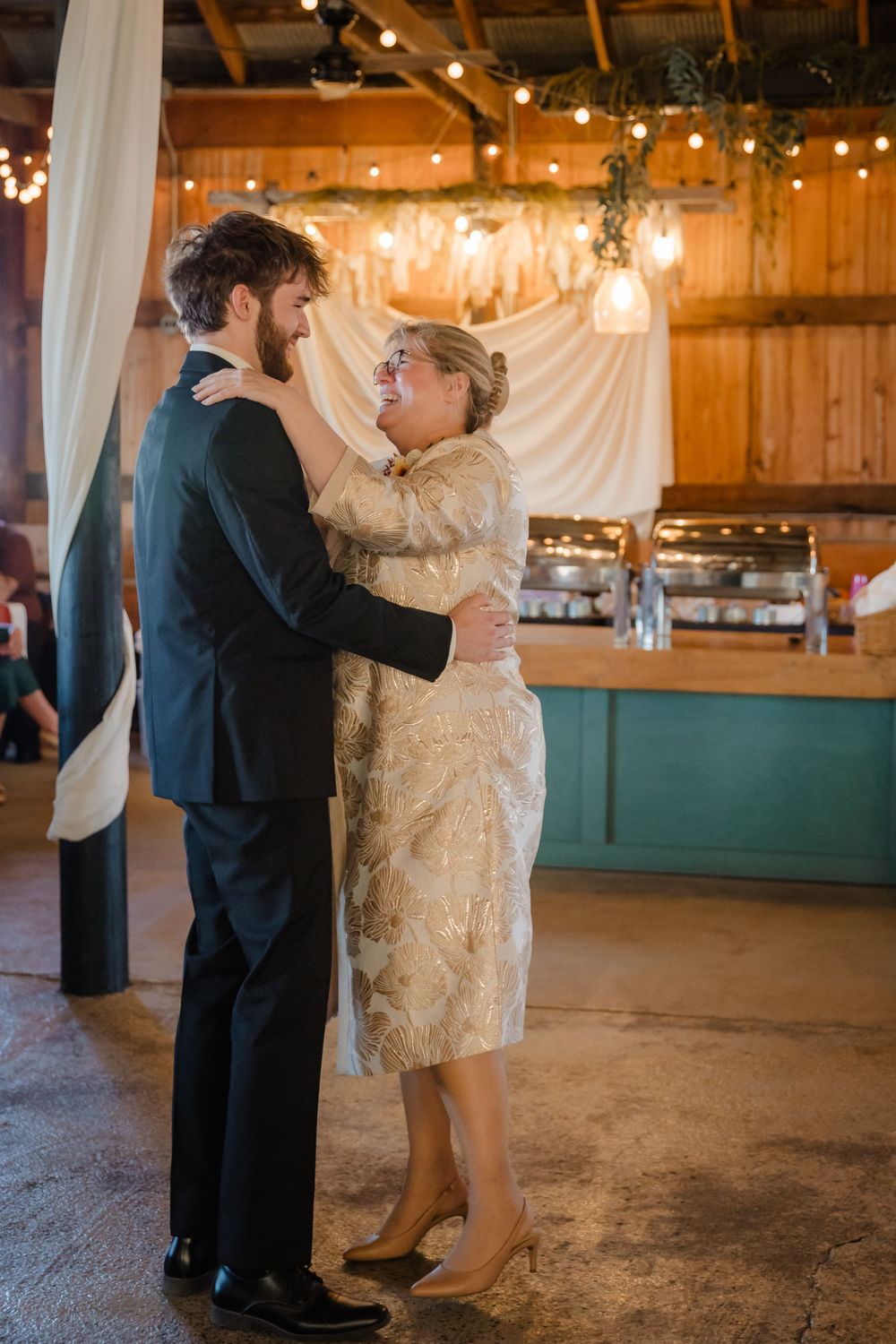 A couple shares a romantic dance moment in a rustic barn venue decorated with twinkling string lights.