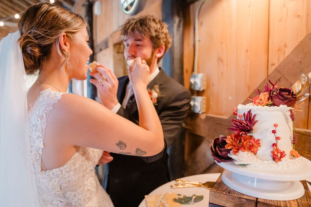 Newlyweds share a sweet moment while cutting their wedding cake together at a rustic reception venue.