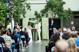 Guests seated at an outdoor wedding ceremony with lush greenery and white floral arrangements.