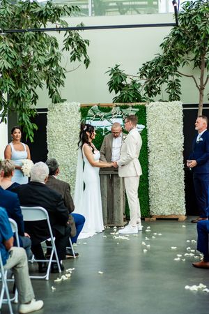 Wedding ceremony in progress with white floral backdrop and scattered rose petals.
