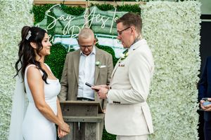 A wedding ceremony moment captured against a white floral wall backdrop.