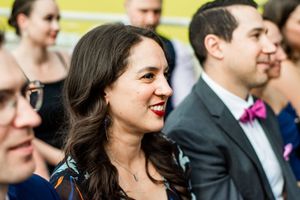 Wedding guests in formal attire smile and interact during an outdoor celebration.