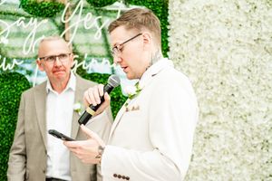 Wedding guests in formal attire gathered against a floral wall backdrop.