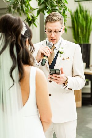 A wedding ceremony moment with participants in white attire surrounded by greenery.