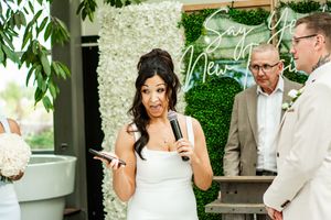 A wedding ceremony in front of a lush green wall with white floral decorations.