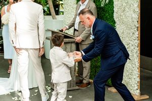 Wedding party members interact during outdoor photo session surrounded by greenery.