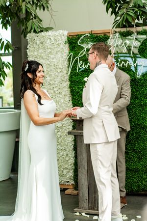 Wedding ceremony taking place in front of an elegant white flower wall backdrop.