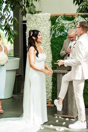 Wedding couple poses for photos in an elegant garden setting with white floral backdrop.