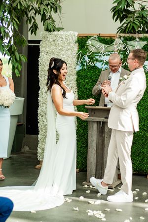 Wedding couple shares a playful dance moment against a green floral wall.