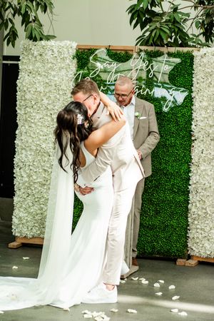 A couple shares a joyful moment during their wedding ceremony in front of a white floral backdrop.