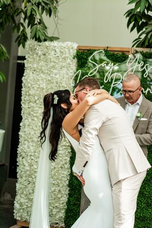 A romantic wedding kiss in front of a decorative white flower wall.
