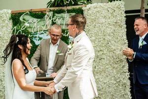 Wedding celebration outdoors with guests mingling against a floral wall backdrop.