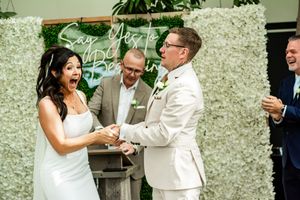 Wedding party in white attire sharing joyful moments together in a garden setting with white floral decorations.
