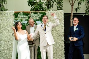 Wedding party members celebrate during an outdoor ceremony with greenery and white decor.