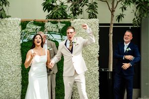 Wedding party celebrating with joyful expressions against a decorative floral wall.