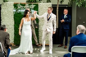 Wedding party members gather for photos in a modern venue with natural greenery.