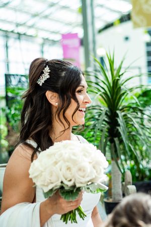 A bride holding a beautiful bouquet of white flowers in a greenhouse setting.