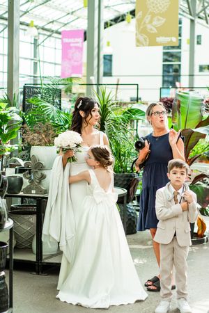 Wedding party members in white and navy attire pose in a bright greenhouse setting.