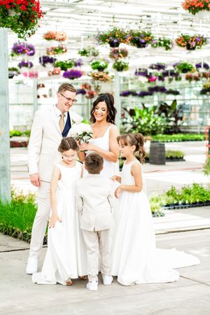 Wedding celebration in a bright greenhouse with hanging flower baskets and white-clad attendees.