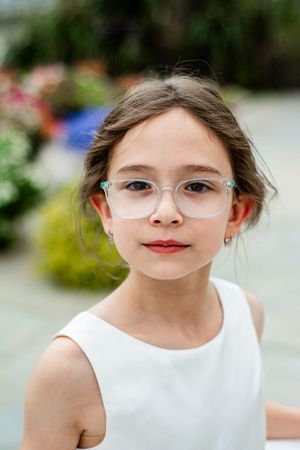 Child in a white sleeveless dress posing in a garden setting.