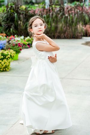 Young child in a white dress twirling in a garden setting.