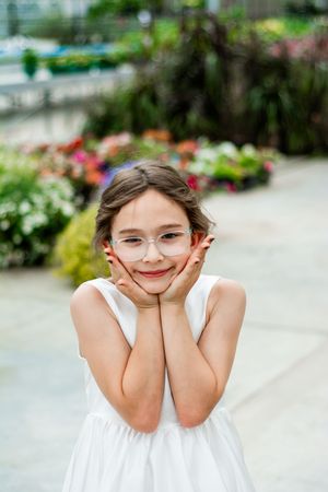Young attendant in white dress poses playfully in a greenhouse garden setting.