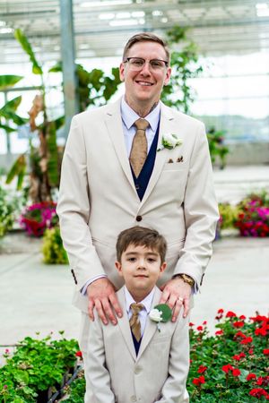 Matching cream suits worn by wedding party members in a greenhouse setting.