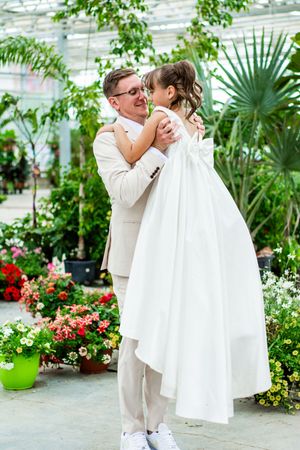 A romantic wedding moment captured in a greenhouse surrounded by lush plants and flowers.