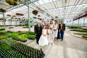 A wedding ceremony setup in a greenhouse with rows of colorful flowers and hanging plants.