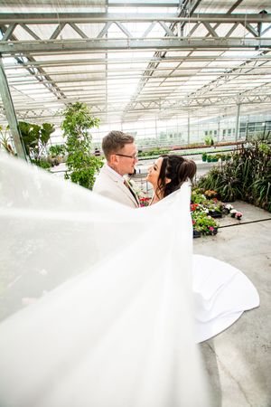 Romantic wedding photoshoot in a sunlit greenhouse with flowing white dress and elegant poses.