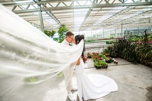A romantic wedding photoshoot in a bright greenhouse with flowing white dress and floral decorations.
