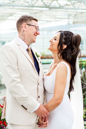 A joyful wedding couple shares intimate moments in a bright greenhouse setting with white attire.