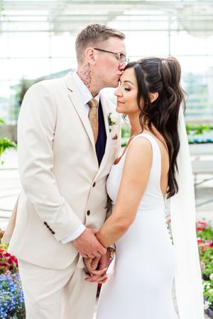 Tender wedding moment photographed in a greenhouse with blooming flowers.