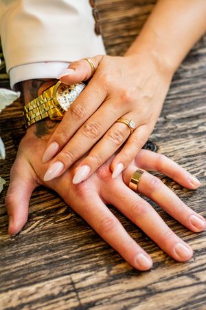 Close-up of hands displaying wedding rings on rustic wooden surface.