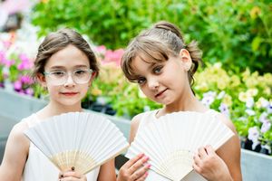 Wedding party members posing with decorative white fans in a garden setting.