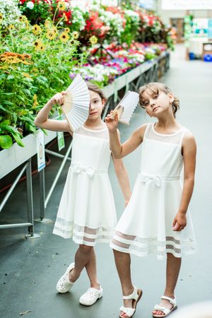 Little girl in white dress twirling and playing in garden center aisle.