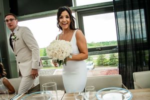 Wedding couple poses together in a modern venue with large windows and white floral arrangements.