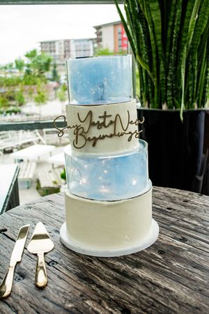 Elegant blue and white wedding cake with delicate script decorations displayed on a weathered wooden table.