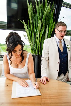People signing documents at a wooden table with tall bamboo plants in the background.