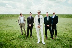 Groomsmen pose together on a green hillside in formal attire.