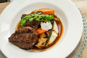 Elegant plated dishes featuring braised meats and vegetables served on white porcelain plates.