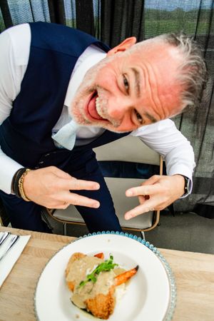 Person in formal attire enthusiastically gestures while presenting plated food at an event.