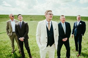 Groomsmen and wedding party members pose on a rolling green hillside.