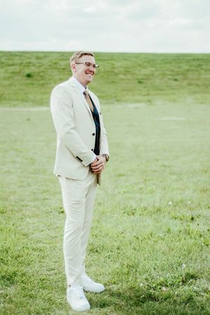 Person in a white suit and tie stands on green grass field during an outdoor event.