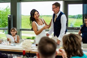 Wedding reception gathering in a bright room with large windows overlooking green landscape.